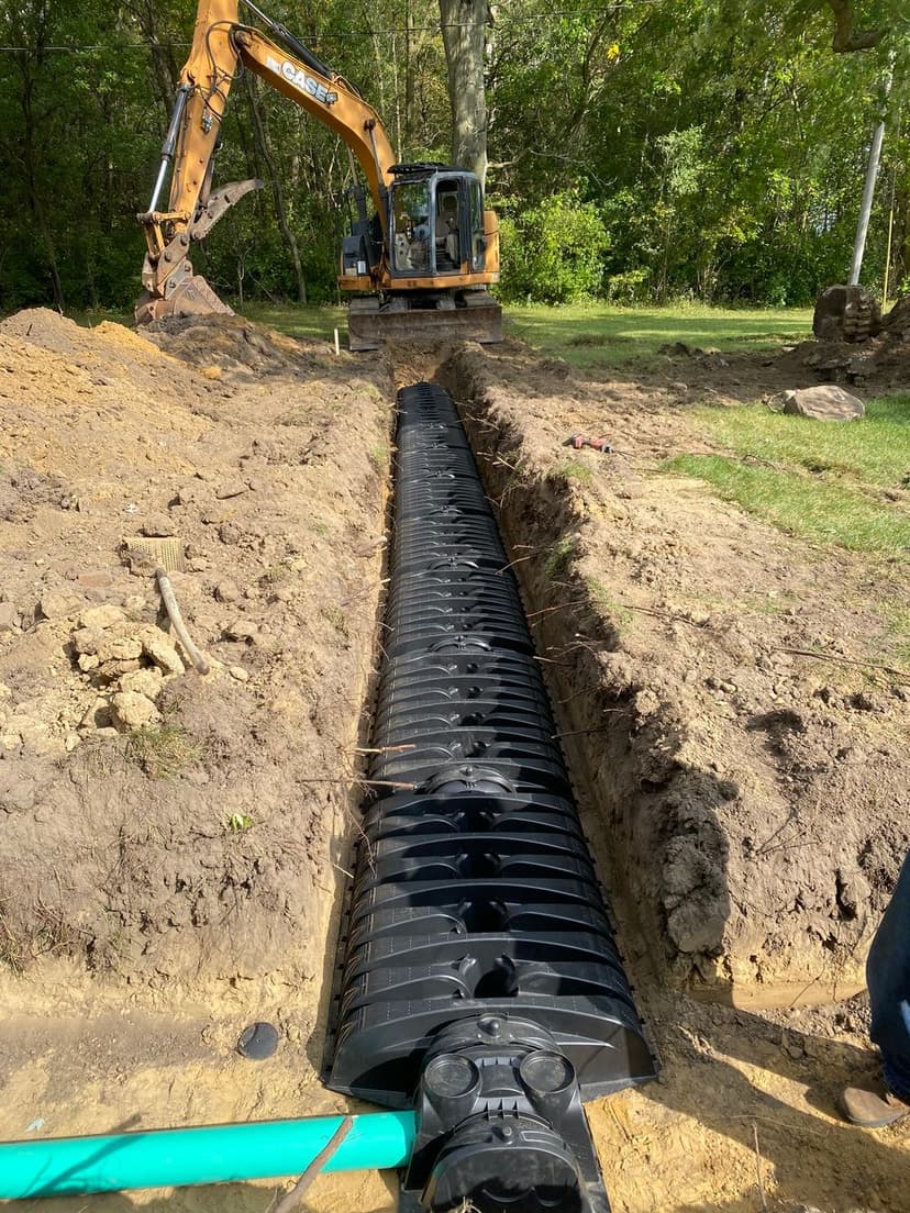 Excavator digging trench for drainage installation with plastic drainage pipes.