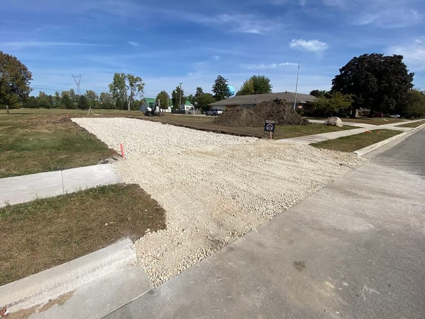 Construction site with gravel driveway on a residential street, surrounded by bare land.