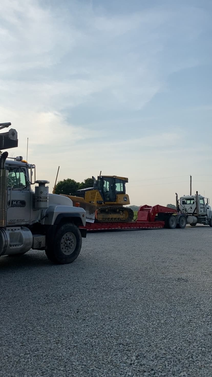 Heavy machinery transport with a yellow bulldozer on a flatbed truck in a gravel lot.
