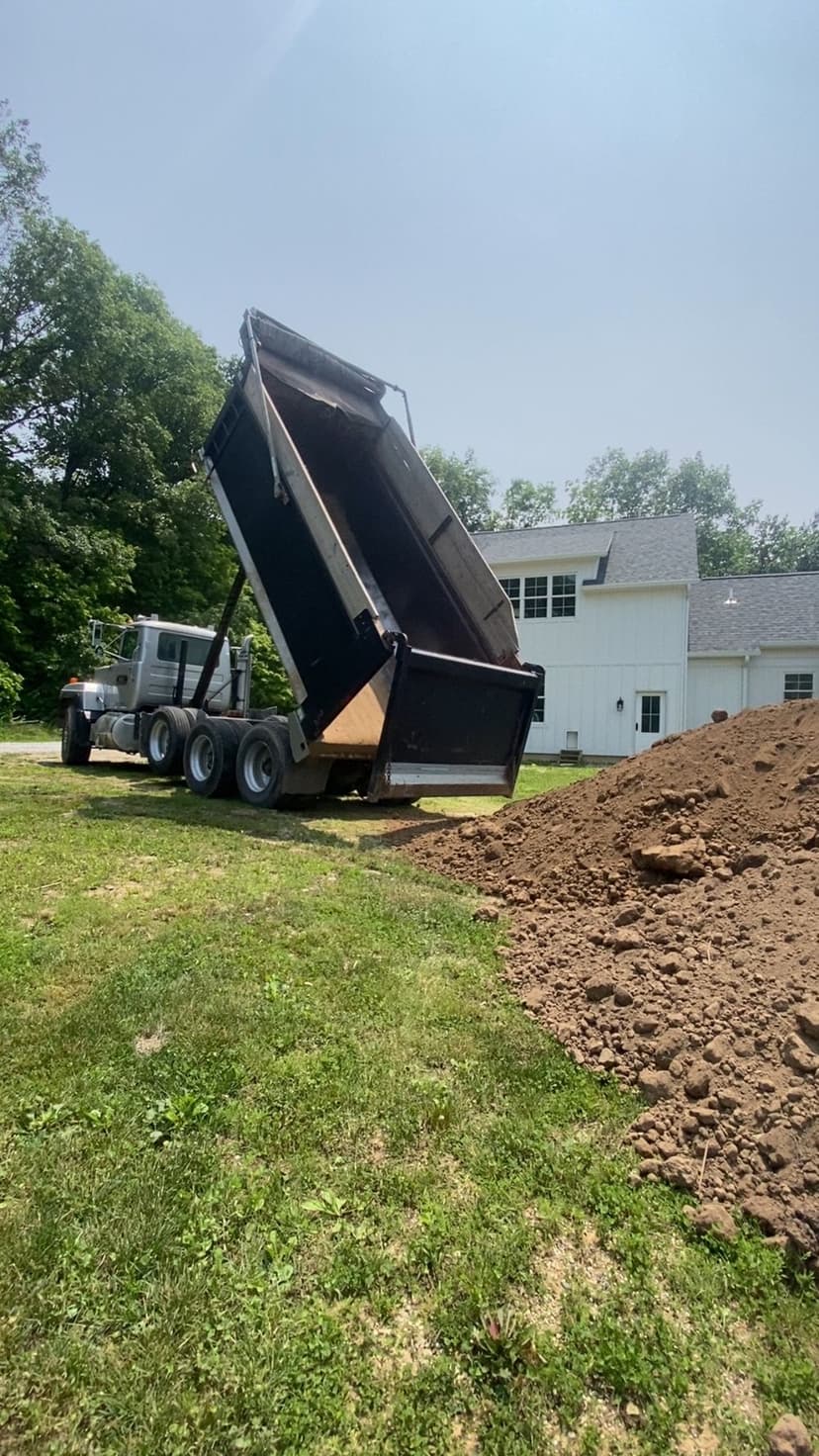 Dump truck unloading dirt near a residential home on a sunny day.