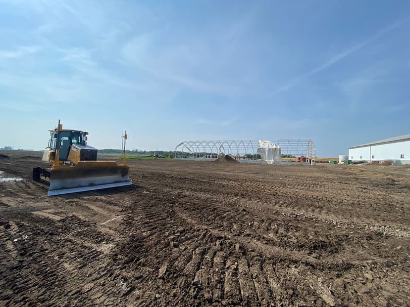 Bulldozer on construction site with new building framework against clear blue sky.