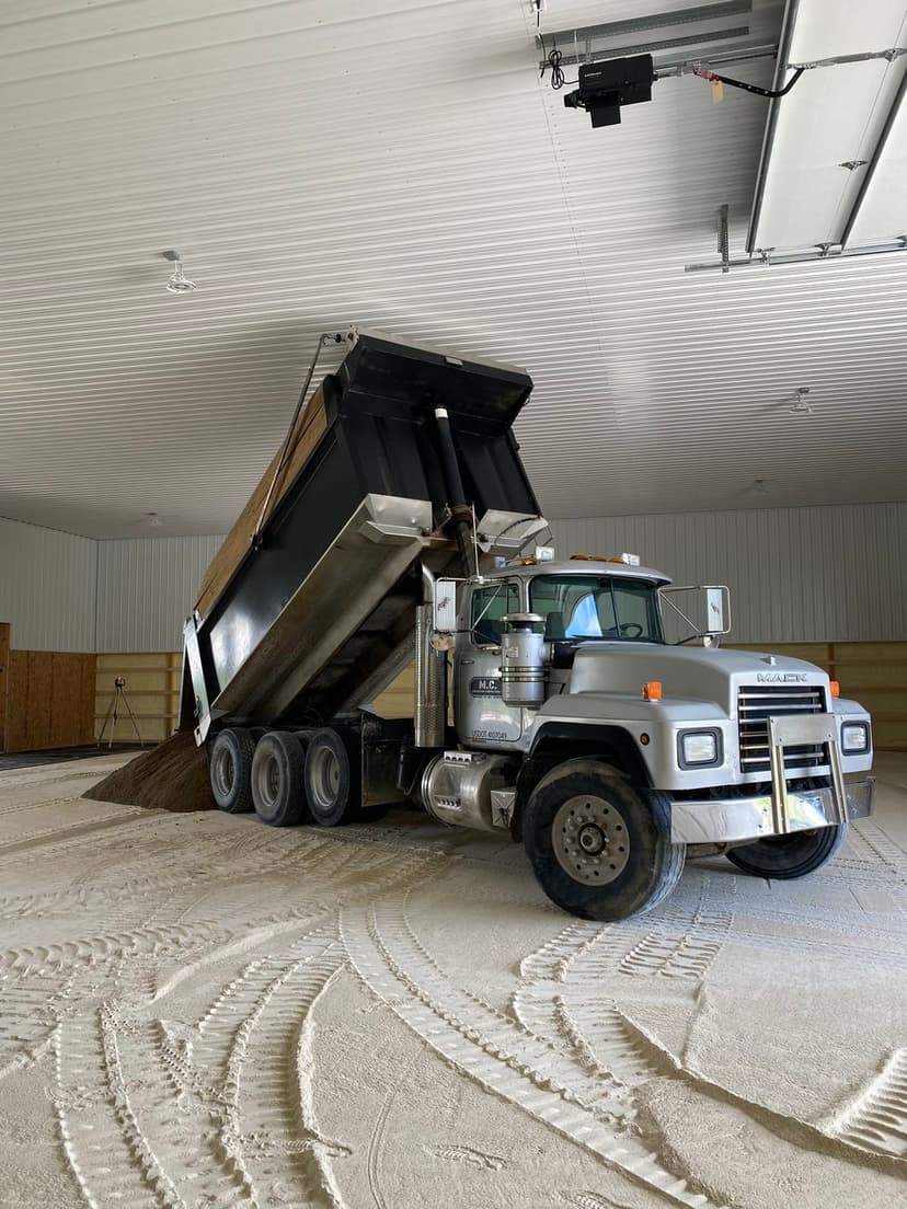 Dump truck unloading gravel in a spacious indoor facility with smooth floor textures.