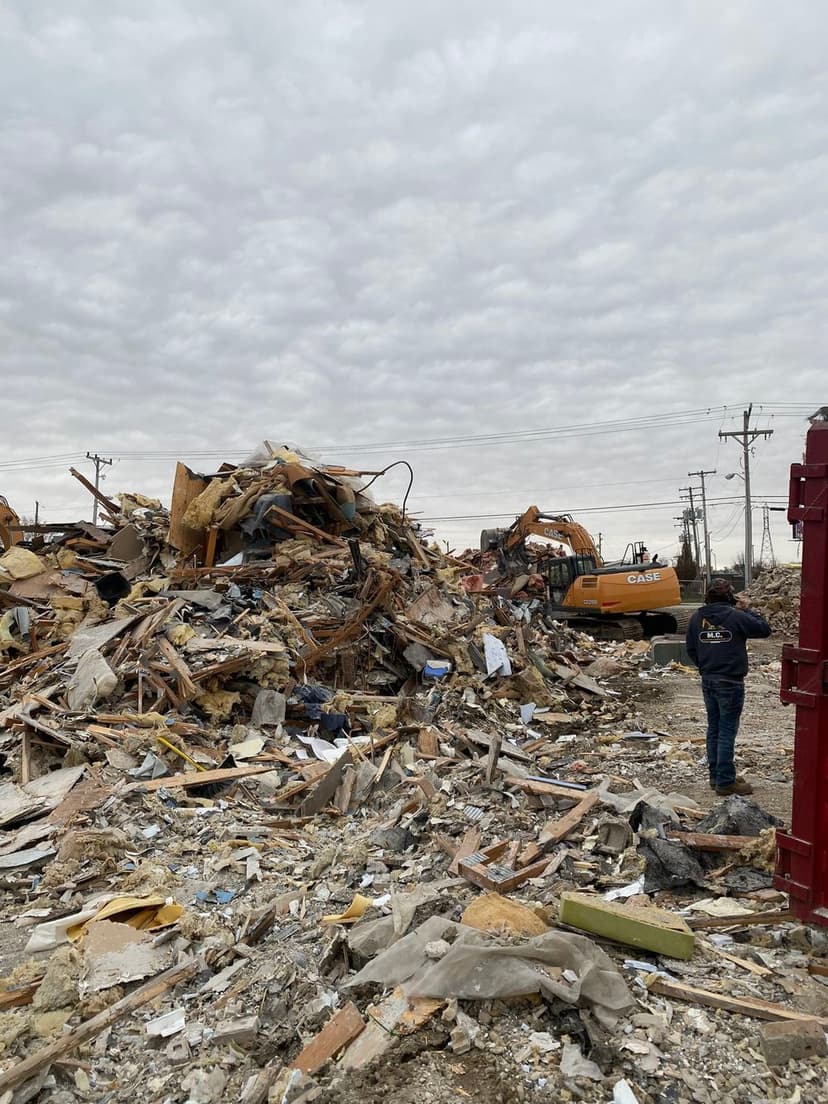 Construction site with heavy machinery clearing rubble and debris under a cloudy sky.
