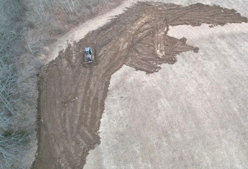 Aerial view of a clearing project showing a tractor on freshly disturbed soil in a field.